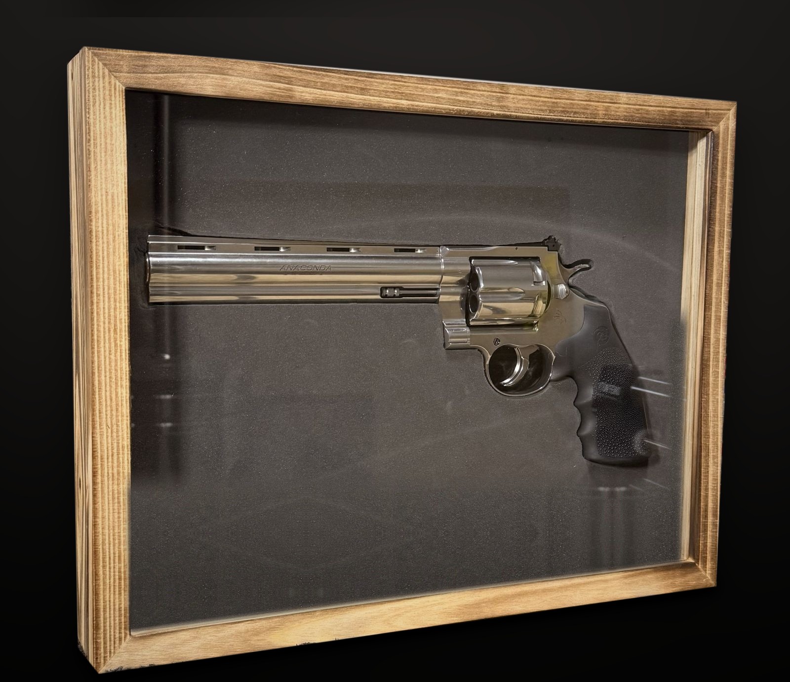 Stainless Colt Anaconda revolver displayed in a wood-framed glass case on black foam